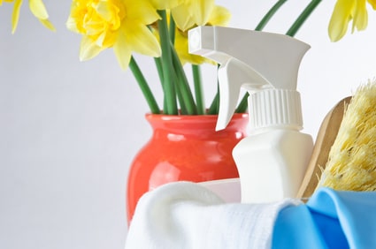 bottle of cleaning spray in a bucket sitting next to a red vase of daffodils