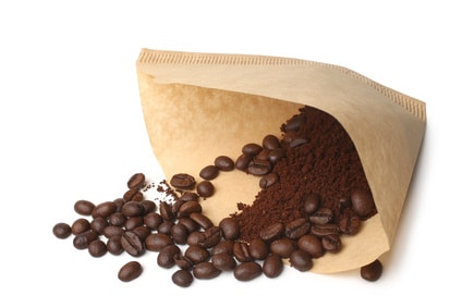 brown coffee filter with coffee beans spilling out on a white background