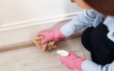 Cleaner wiping baseboards and floor edges inside a home.